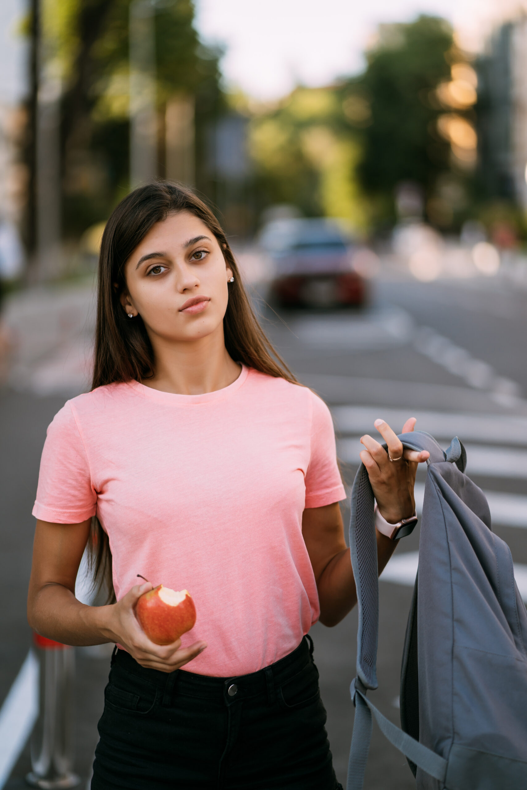 Portrait of a young woman holding apple against a street background